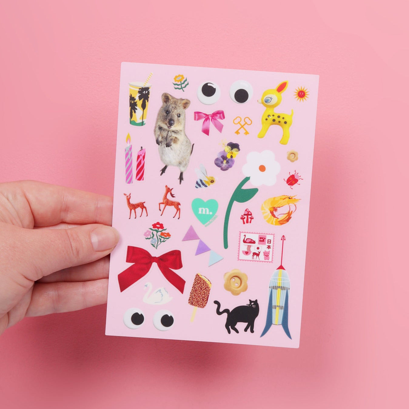 Hand holding a sheet of colorful stickers against a pink background