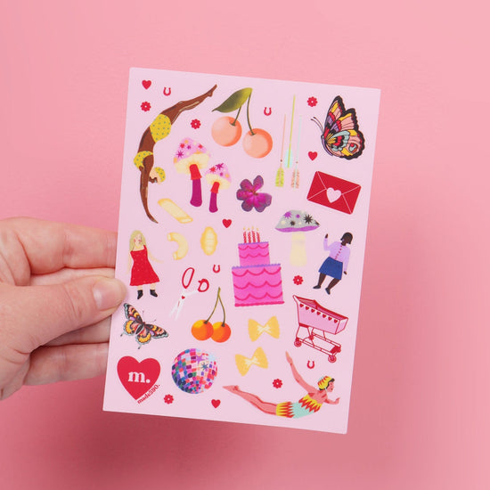 Hand holding a colorful sticker sheet against a pink background