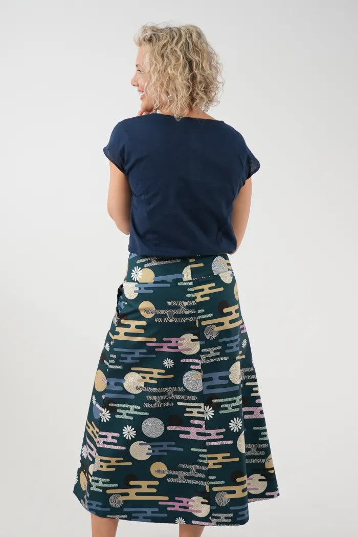 A woman shown from the back wearing a navy blue short-sleeve top and a dark teal A-line skirt with a colorful abstract pattern 