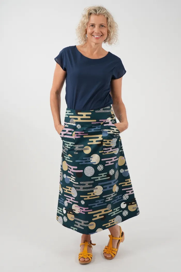 A woman modeling a navy blue short-sleeve top and a dark teal A-line midi skirt with a colorful geometric pattern 