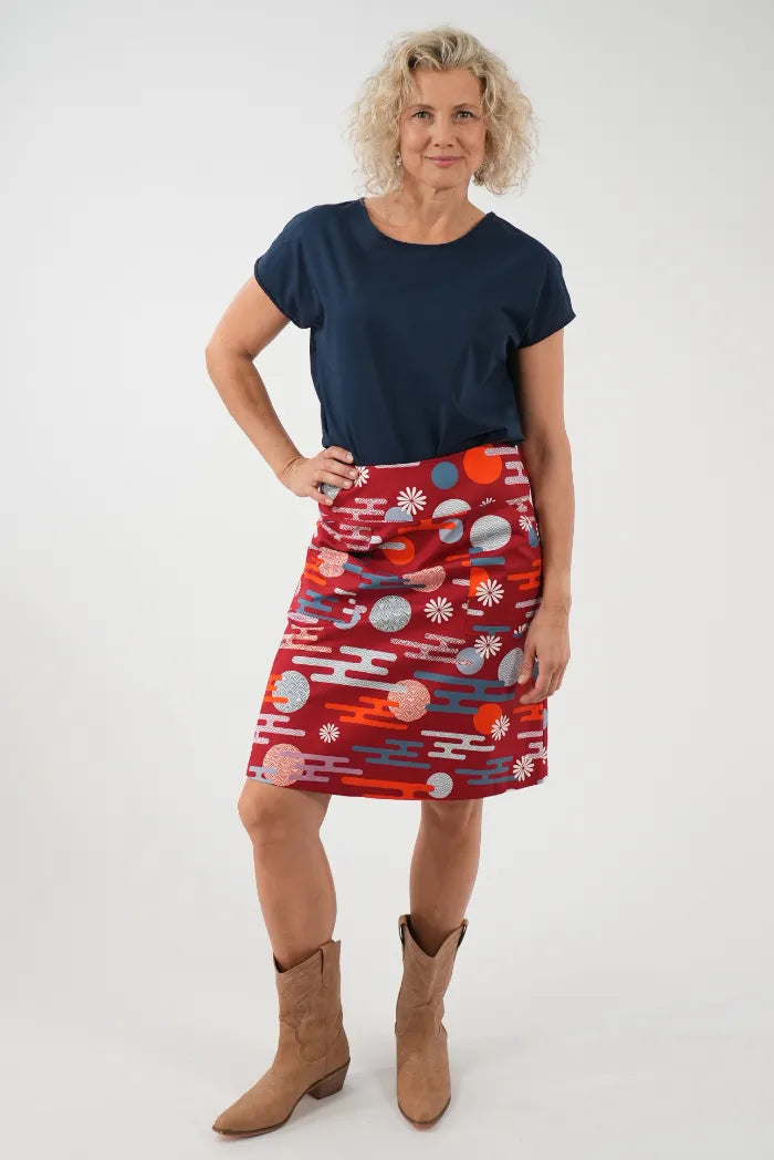 A woman modeling a red wrap-style skirt with a colorful abstract pattern, 