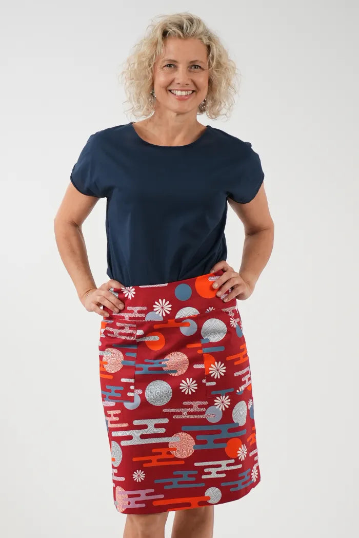 A woman modeling a red knee-length skirt with a colorful abstract pattern of circles, waves, 