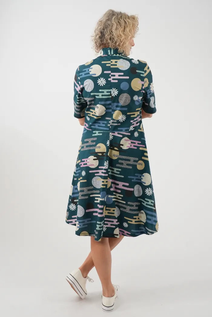 A woman viewed from behind wearing a dark teal midi dress with a colorful retro pattern 