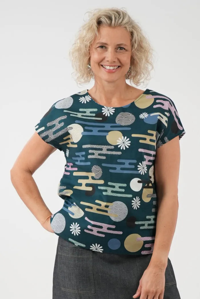 wearing a short-sleeve crewneck top with a multicolor abstract pattern on a dark teal background, 